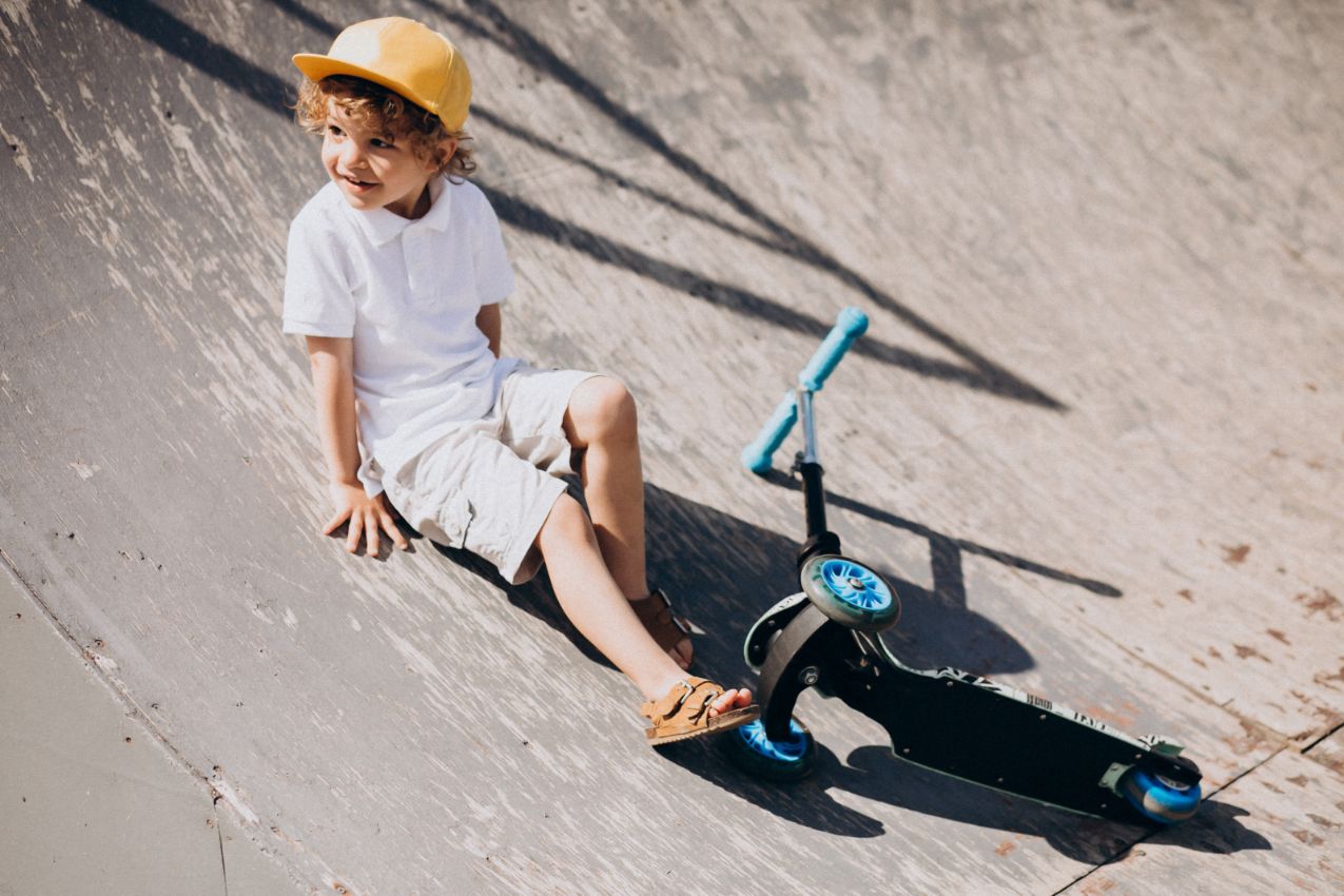 کودکی در پارک مخصوص اسکوتر سواری در حال لبخند زدن به همراه اسکوتری در کنارش